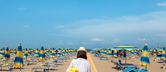 Spiaggia con ombrelloni gialli e blu, madre e figlia camminano.